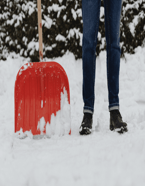 A person standing in snow holding a red shovel.